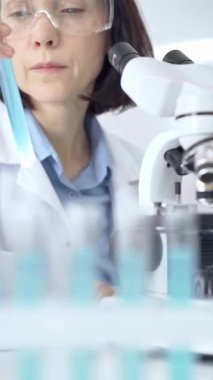 Odaklanmış kadın araştırmacı modern bir laboratuvar ortamında temiz bir test tüpünü inceliyor.