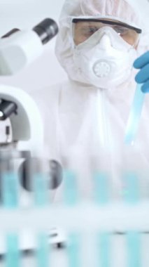 Profesyonel bilim adamı, mikroskobun yanındaki tüp örneğini dikkatlice analiz ediyor.
