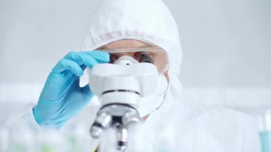 Koruyucu ekipman kullanan profesyonel bilim adamı laboratuvar ortamında mikroskop kullanıyor..