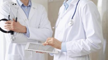 Dijital tablet kullanan, beyaz önlük ve steteskop giyen iki doktor bir hastanın tıbbi geçmişini tartışıyor. Tıp ve Bilim.