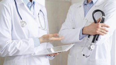Dijital tablet kullanan, beyaz önlük ve steteskop giyen iki doktor bir hastanın tıbbi geçmişini tartışıyor. Tıp ve Bilim.