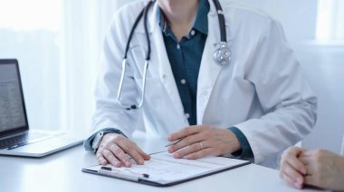 Doktor ve bir hasta. Yeşil bir gömleğin üzerine beyaz bir sağlık önlüğü giyen hekim klinikteki muayene sırasında elleriyle işaret ediyor. İlaç..