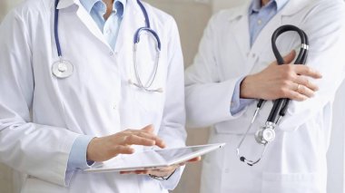 Dijital tablet kullanan, beyaz önlük ve steteskop giyen iki doktor bir hastanın tıbbi geçmişini tartışıyor. Tıp ve Bilim.