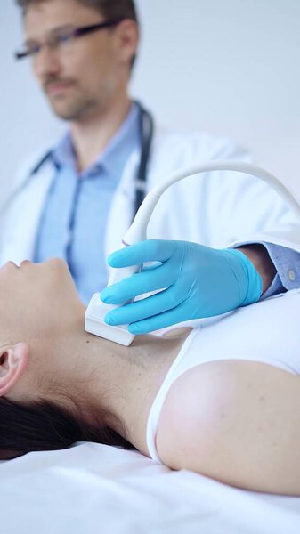 Врач в синих защитных перчатках использует ультразвуковую машину для обследования шеи пациентки в клинике. Медицина, исследование щитовидной железы.