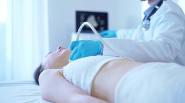 Mavi eldivenli doktor, klinik prosedür dolabında yatan kadın hastanın boynunu incelemek için ultrason makinesi kullanıyor. İlaç servisi..