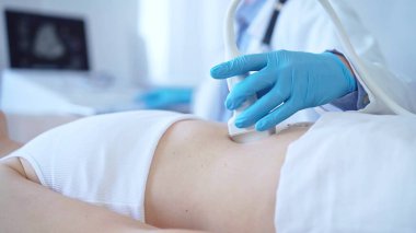 Doktor, klinikte yatan bir kadın hastaya ultrason cihazıyla mavi eldiven takıyor. Tıp konsepti.