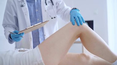Mavi tıbbi eldiven giyen doktor, bir klinikte tıbbi muayene sırasında hastaların dizlerini muayene eder. Tıp ve ortopedi kavramı..