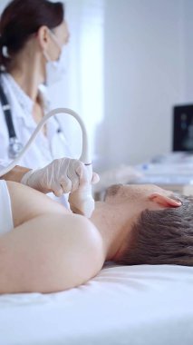 Beyaz tıbbi eldivenli doktor kadın erkek hastaya boyun ultrasonu yapıyor. Tiroid bezi muayenesi. Tıp konsepti.