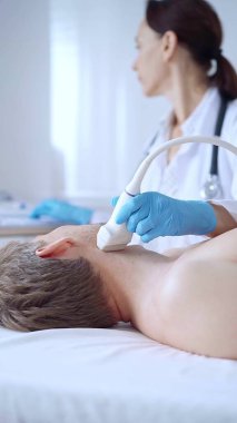Doktor kadın mavi eldiven giyip erkek hastaya boyun ultrasonu yapıyor. Tıp hizmeti kavramı.