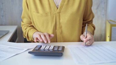 Sarı mavisi olan iş kadını karanlık hesap makinesi kullanıyor ve ofisinde not alıyor. İş hayatında vergiler ve denetim.