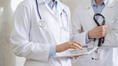 Dijital tablet kullanan, beyaz önlük ve steteskop giyen iki doktor bir hastanın tıbbi geçmişini tartışıyor. Tıp ve Bilim.