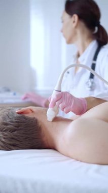 Pembe tıbbi eldivenli doktor kadın erkek hastaya boyun ultrasonu yapıyor. Tiroid bezi muayenesi. Tıp konsepti.