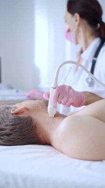 Pembe tıbbi eldivenli doktor kadın erkek hastaya boyun ultrasonu yapıyor. Tiroid bezi muayenesi. Tıp konsepti.