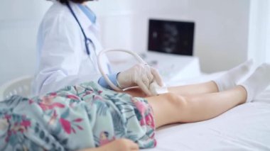 Doktor ve çocuk hasta. Ortopedist, beyaz koruyucu eldivenler giyip bir klinikte çocuğun dizinde ultrason muayenesi yapıyor..