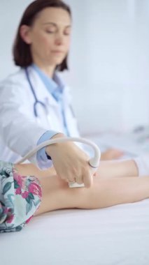 Doktor ve çocuk hasta. Bir klinikte ortopedist bir çocuğun dizinde ultrason muayenesi yapıyor. İlaç ve sağlık hizmetleri.