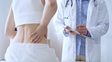 Doktor adam, hasta kadın sırt ağrısından bahsederken bir not panosuna not alıyor. Tıp ve ortopedi kavramları.