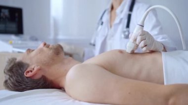 Beyaz koruyucu eldivenli doktor kadın klinik prosedür dolabında yatan erkek göğüs röntgeni çekiyor. Kardiyoloji teşhisi ve tıp hizmeti kavramı.