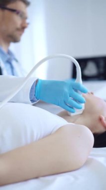 Mavi koruyucu eldiven giyen doktor, klinikteki kadın hastayı muayene etmek için ultrason makinesi kullanıyor. İlaç, tiroit bezi muayenesi..