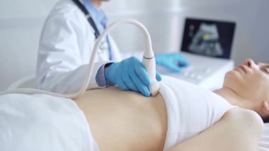 Mavi tıbbi eldiven giyen doktor, tıbbi kardiyoloji muayenesi için uzanan bir kadının göğsünde ultrason cihazı kullanıyor. Tıp konsepti.