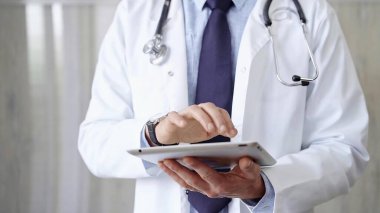 Laboratuvar önlüğü ve steteskop giyen doktor hastanede tablet bilgisayar kullanıyor. Tıp ve Bilim.