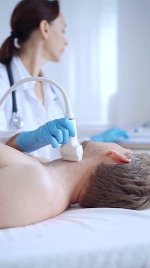 Doktor kadın mavi eldiven giyip erkek hastaya boyun ultrasonu yapıyor. Tıp hizmeti kavramı.