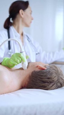 Yeşil eldivenli doktor kadın erkek hastaya boyun ultrasonu yapıyor. Tiroid bezi muayenesi. Tıp konsepti.