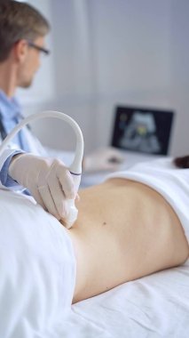 Doctor man wearing white protective gloves is using ultrasound equipment on the back of a patient, woman. The results are on a monitor in the background. Medicine service. clipart