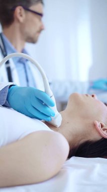 Mavi koruyucu eldiven giyen doktor, klinikteki kadın hastayı muayene etmek için ultrason makinesi kullanıyor. İlaç, tiroit bezi muayenesi..