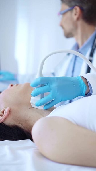 Врач в синих защитных перчатках использует ультразвуковую машину для обследования шеи пациентки в клинике. Медицина, исследование щитовидной железы.