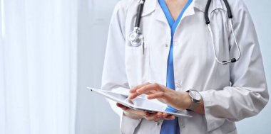 Doktor kadın klinikte dijital tablet kullanıyor. Steteskoplu bir sağlık uzmanı ayakta dururken dokunmatik ekran tableti kullanıyor..