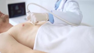 Erkek hastaya göğüs ve kalp ultrasonu uygulayan beyaz tıbbi eldiven giyen doktor kadın. Tıp hizmeti, kardiyoloji.
