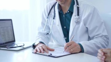 Doktor ve bir hasta. Yeşil gömleğin üzerine beyaz bir tıbbi önlük giyen hekim klinikteki muayene sırasında tıbbi kayıt formu dolduruyor. Tıbbi hizmet.