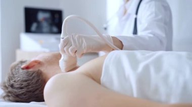 Doktor kadın beyaz önlük giyip erkek hastaya boyun ultrasonu yapıyor. Tıp hizmeti kavramı.