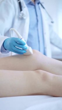 Kadın bir hastanın dizinde ultrason cihazı kullanan mavi koruyucu eldivenli bir erkek doktor. Tıp konsepti.