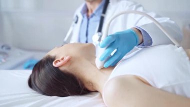 Mavi tıbbi eldiven giyen doktor kadın hastanın boynunda ultrason cihazı kullanıyor. Tıbbi muayene için uzanmış..
