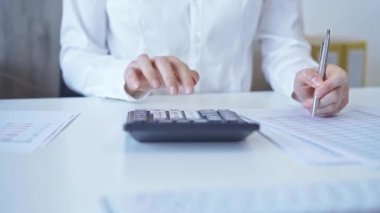 Beyaz mavisi olan iş kadını karanlık hesap makinesi kullanıyor ve ofisinde not alıyor. İş hayatında vergiler ve denetim.