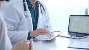 Doktor ve bir hasta. Yeşil gömleğin üzerine beyaz bir tıbbi önlük giyen hekim klinikteki muayene sırasında tablet bilgisayar kullanıyor. Tıp konsepti.
