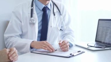 Doktor ve bir hasta. Doktor, mavi gömlek ve kravatın üzerine beyaz bir ceket giyiyordu. Klinikteki muayene sırasında elleriyle el kol hareketi yapıyordu. Tıp konsepti
