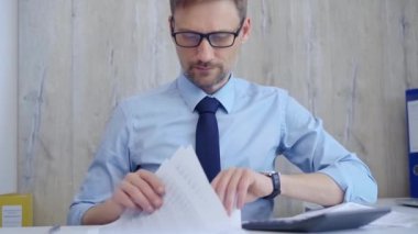 Masrafları hesaplarken ve masasında notlar alırken mavi tişörtlü bir erkek muhasebeci. Vergiler, iş denetimleri.