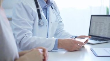 Doktor ve bir hasta. Mavi gömleğin üzerine beyaz bir tıbbi önlük giyen hekim klinikteki muayene sırasında tablet bilgisayar kullanıyor. Tıp ve Bilim.