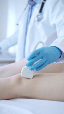 Kadın bir hastanın dizinde ultrason cihazı kullanan mavi koruyucu eldivenli bir erkek doktor. Tıp konsepti.