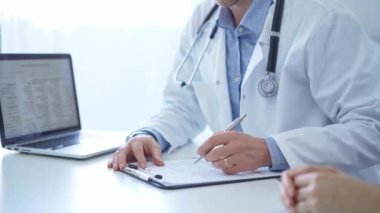 Bir doktor ve bir hasta. Mavi bir gömleğin üzerine beyaz bir ceket giyen hekim klinikteki muayene sırasında tıbbi kayıt formu dolduruyor. Tıbbi hizmet.