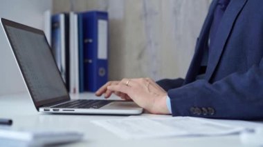 Mavi takım elbiseli bir iş adamı laptopuyla ofisteki klavyede daktilo çalıyor. İş konsepti.