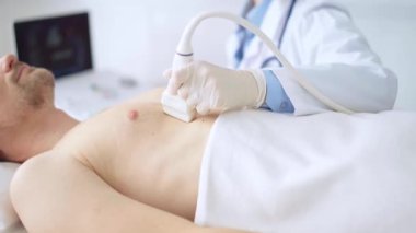 Erkek hastaya göğüs ve kalp ultrasonu uygulayan beyaz tıbbi eldiven giyen doktor kadın. Tıp hizmeti, kardiyoloji.