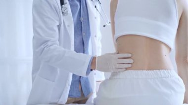 Doktor adam beyaz eldivenler giyip klinikteki kadın hastayı muayene ediyor. Tıp ve ortopedi kavramları.