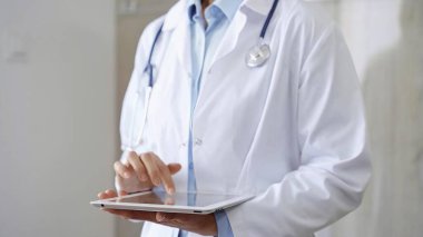 Doktor kadın laboratuvar önlüğü ve steteskop giyiyordu. Hastanede tablet bilgisayar kullanıyordu. Tıp ve bilim konsepti.