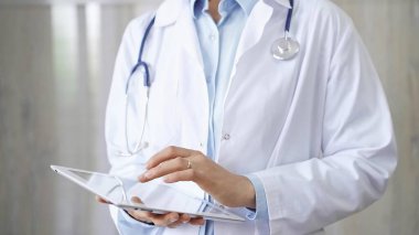 Doktor kadın laboratuvar önlüğü ve steteskop giyiyordu. Hastanede tablet bilgisayar kullanıyordu. Tıp ve bilim konsepti.