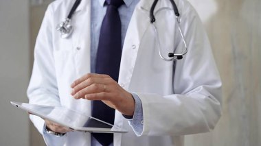 Laboratuvar önlüğü ve steteskop giyen doktor hastanede tablet bilgisayar kullanıyor. Tıp ve Bilim.