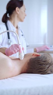 Pembe tıbbi eldivenli doktor kadın erkek hastaya boyun ultrasonu yapıyor. Tiroid bezi muayenesi. Tıp konsepti.