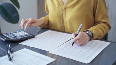 Sarı bluzlu profesyonel iş kadını mali raporlar üzerinde çalışıyor. Bir kadının hesap makinesini hesap denetimi ya da muhasebesi için kullanarak ellerini yakınlaştır.
